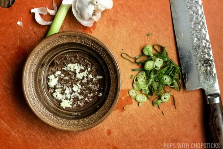 Green onions finely chopped on a cutting board with grated garlic