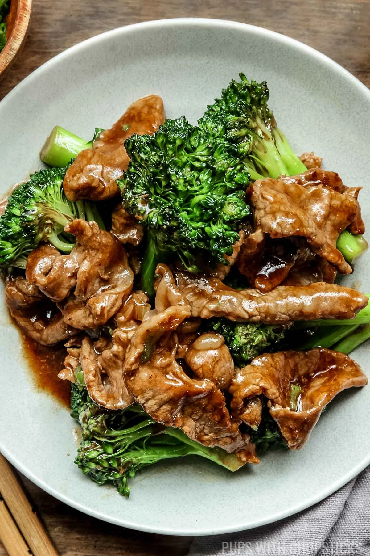 chinese beef and broccoli on a grey plate with wooden chopsticks.