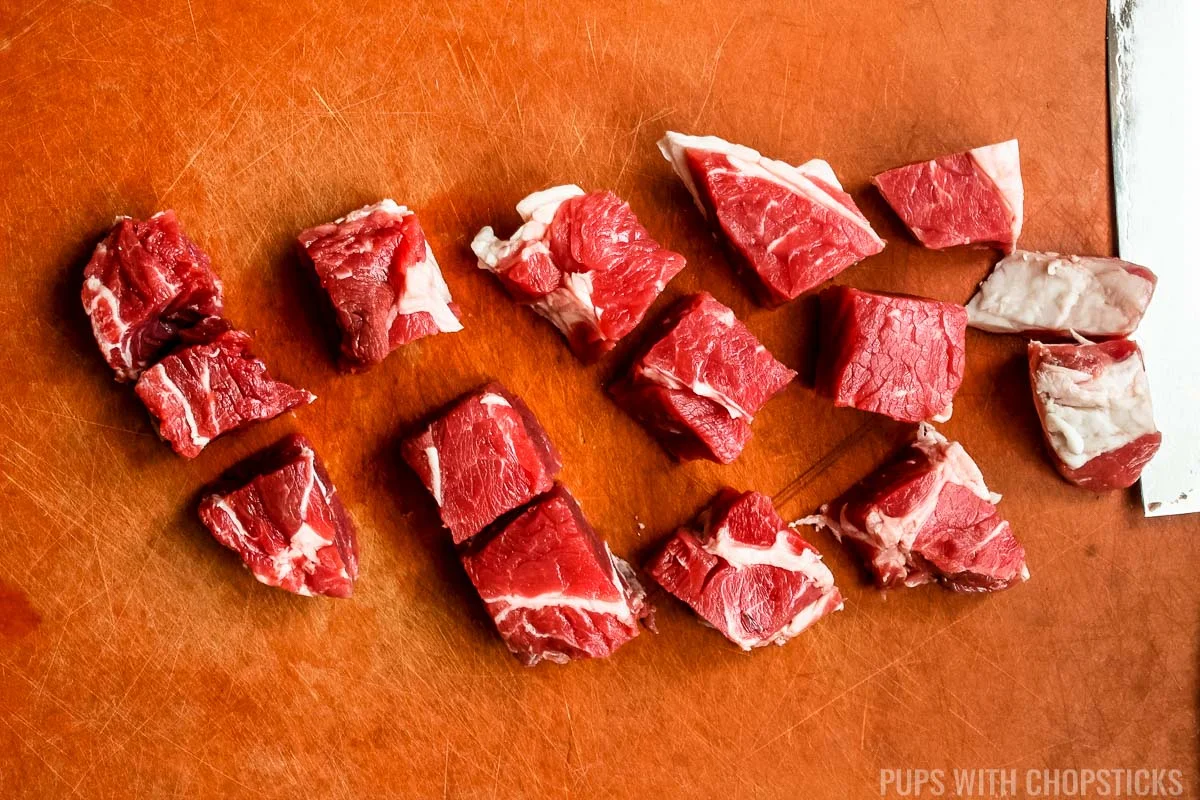 rib eye steak cut into 1 inch cubes on a cutting board.