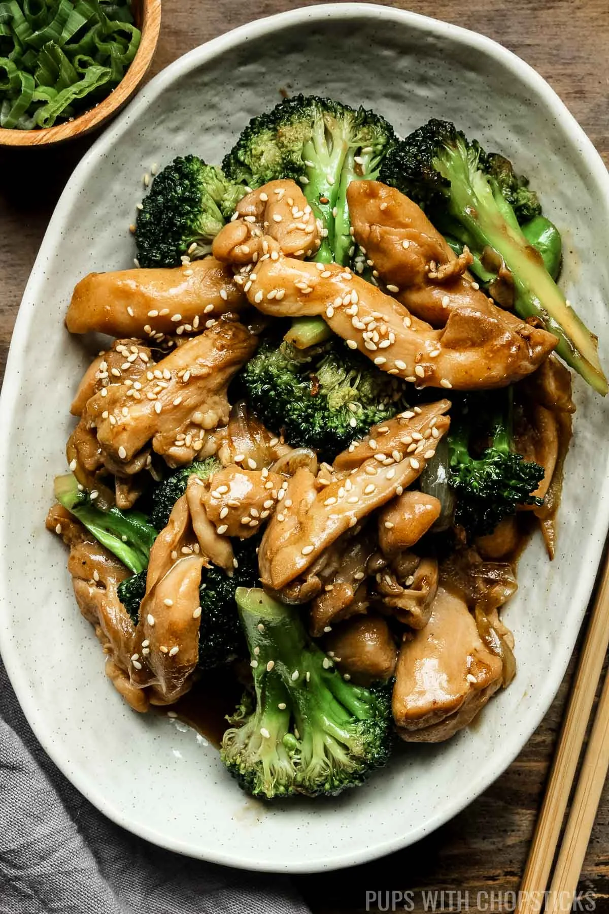 chinese chicken and broccoli stir fry on a white plate on a wooden table.