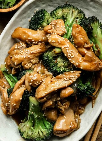 chinese chicken and broccoli stir fry on a white plate on a wooden table.