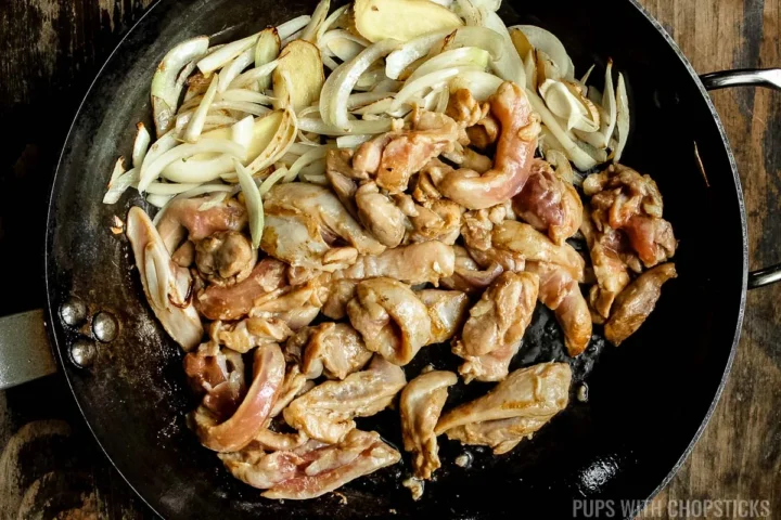 chicken being cooked with onions in a frying pan.