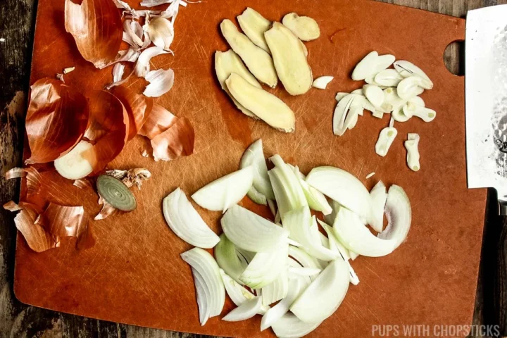 garlic, ginger and onion slices on a cutting board.