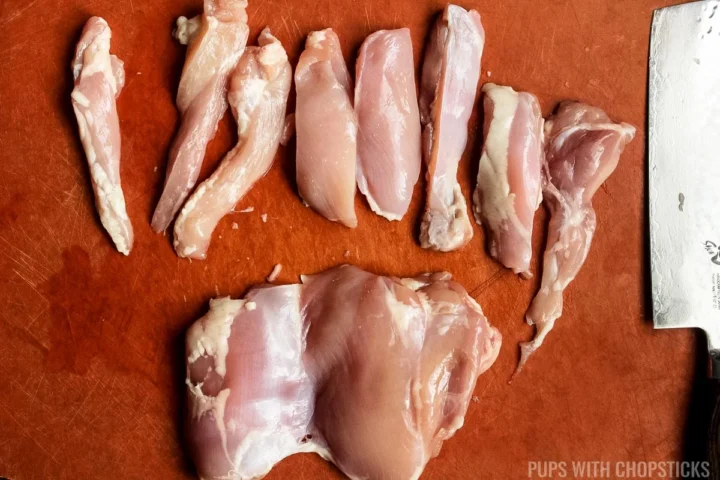 chicken being cut into long strips on a cutting board.
