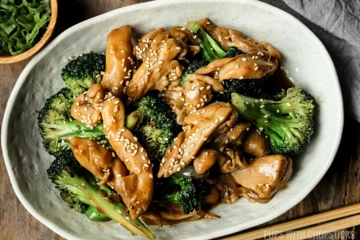 chicken and broccoli stir fry with wooden chopsticks on the side on a white plate.