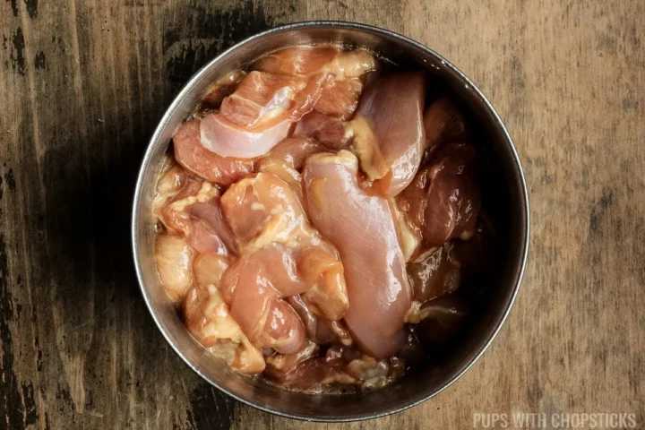 Chicken pieces being marinated in a metal bowl.