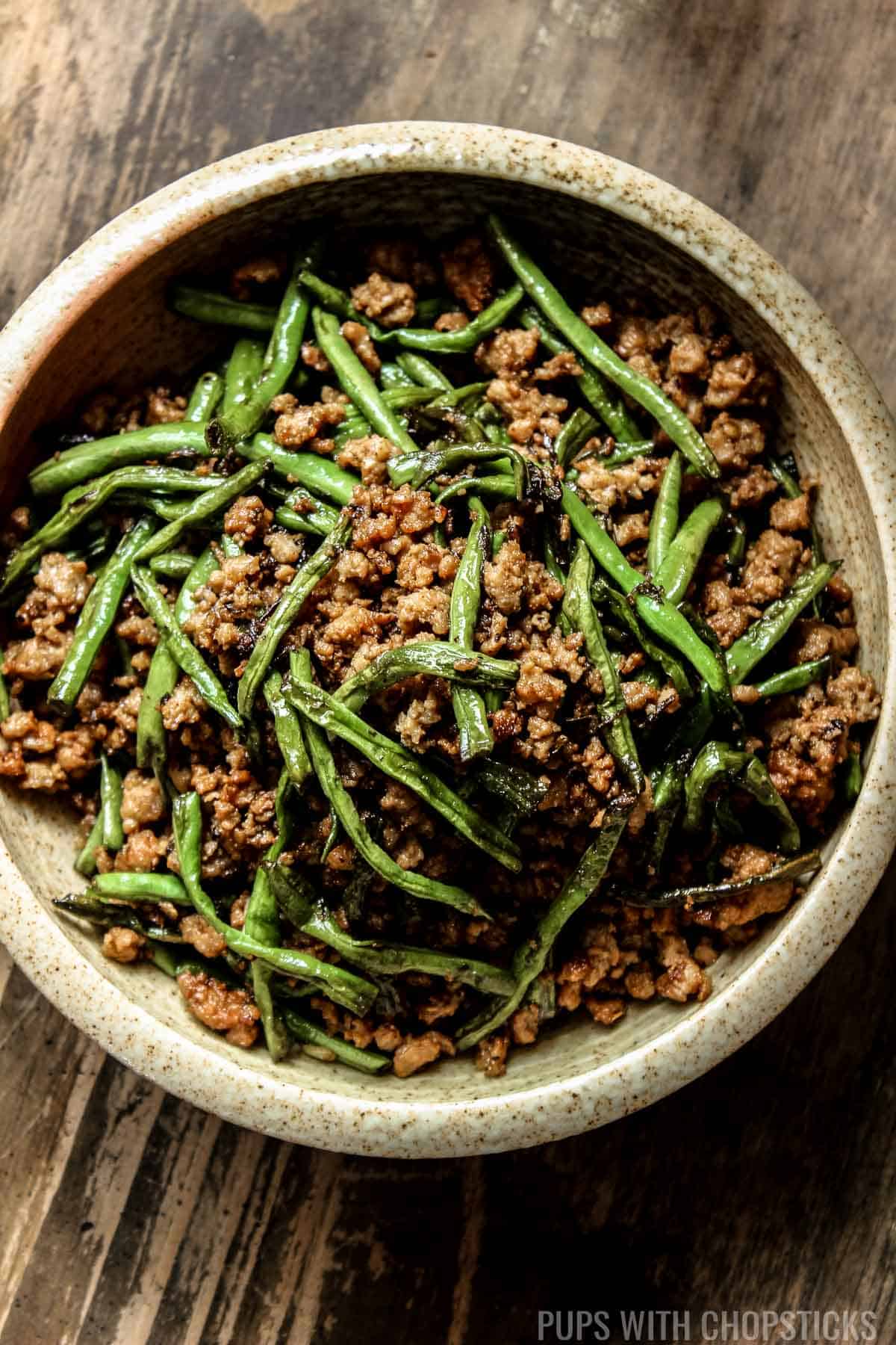 Close up of Dry-Fried Long Beans and Minced Pork with Olive Vegetables in a beige bowl