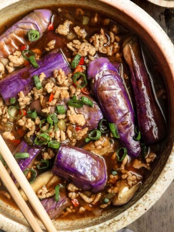 Overhead closeup picture of Chinese eggplant with garlic sauce in a large bowl with green onions on top