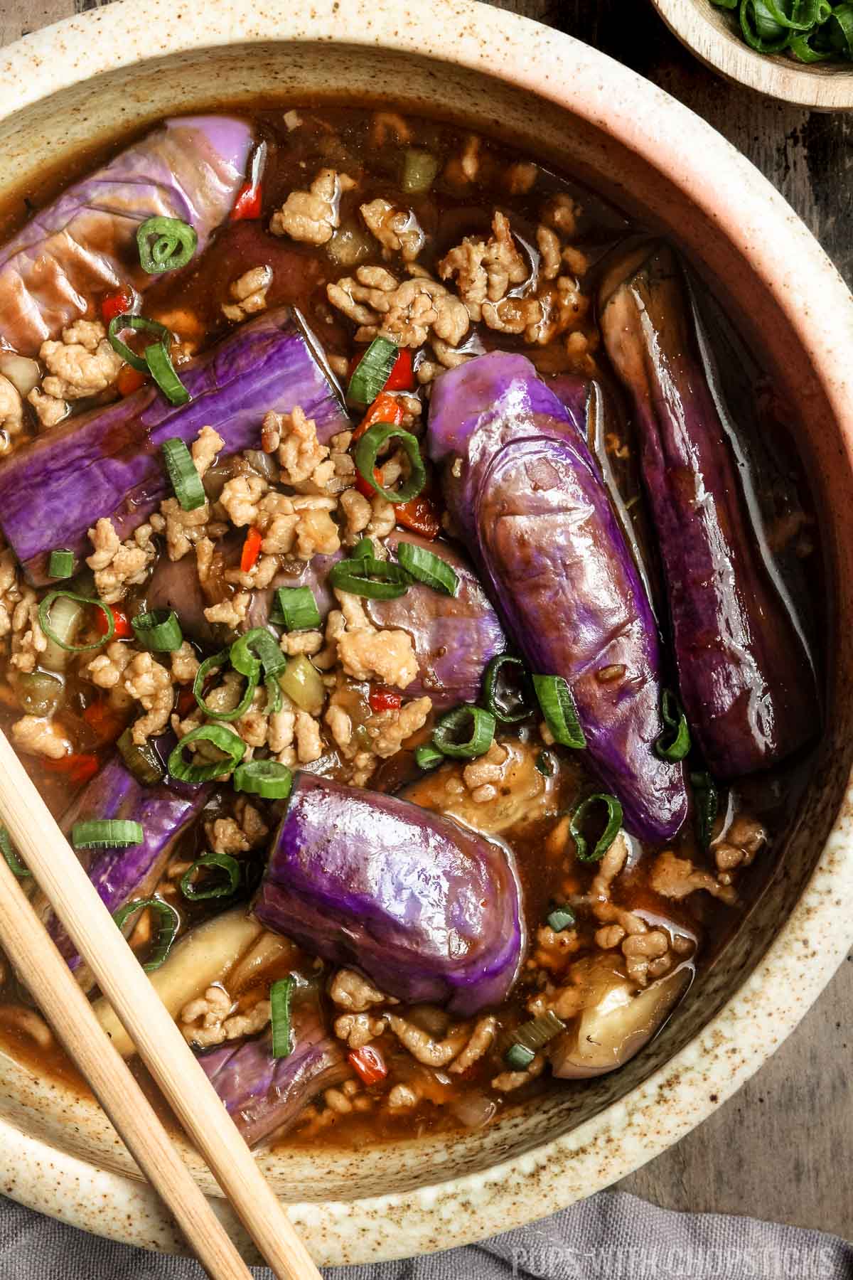 Overhead closeup picture of Chinese eggplant with garlic sauce in a large bowl with green onions on top