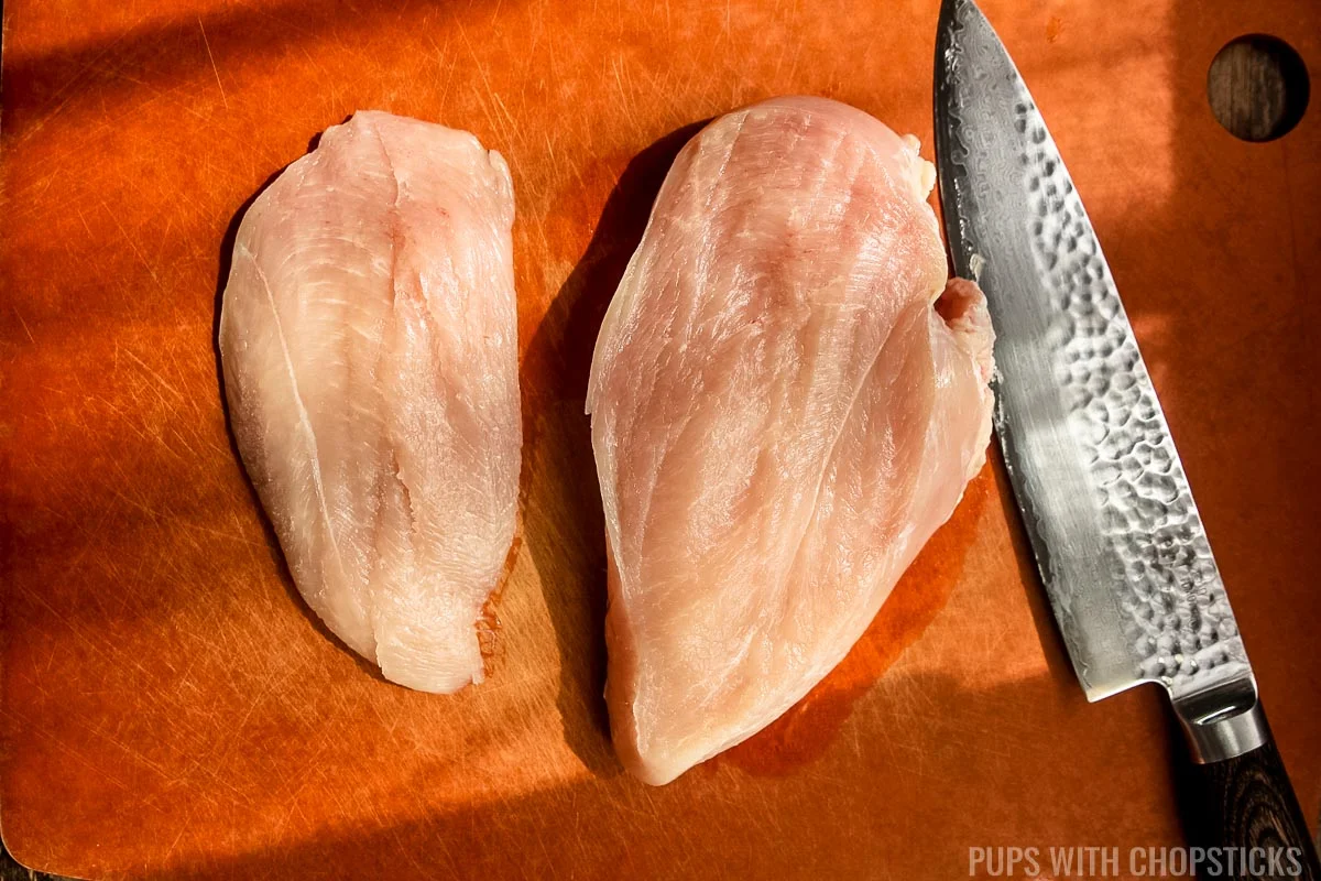 A thin slice of raw chicken breast cut into a thin filet on a cutting board.
