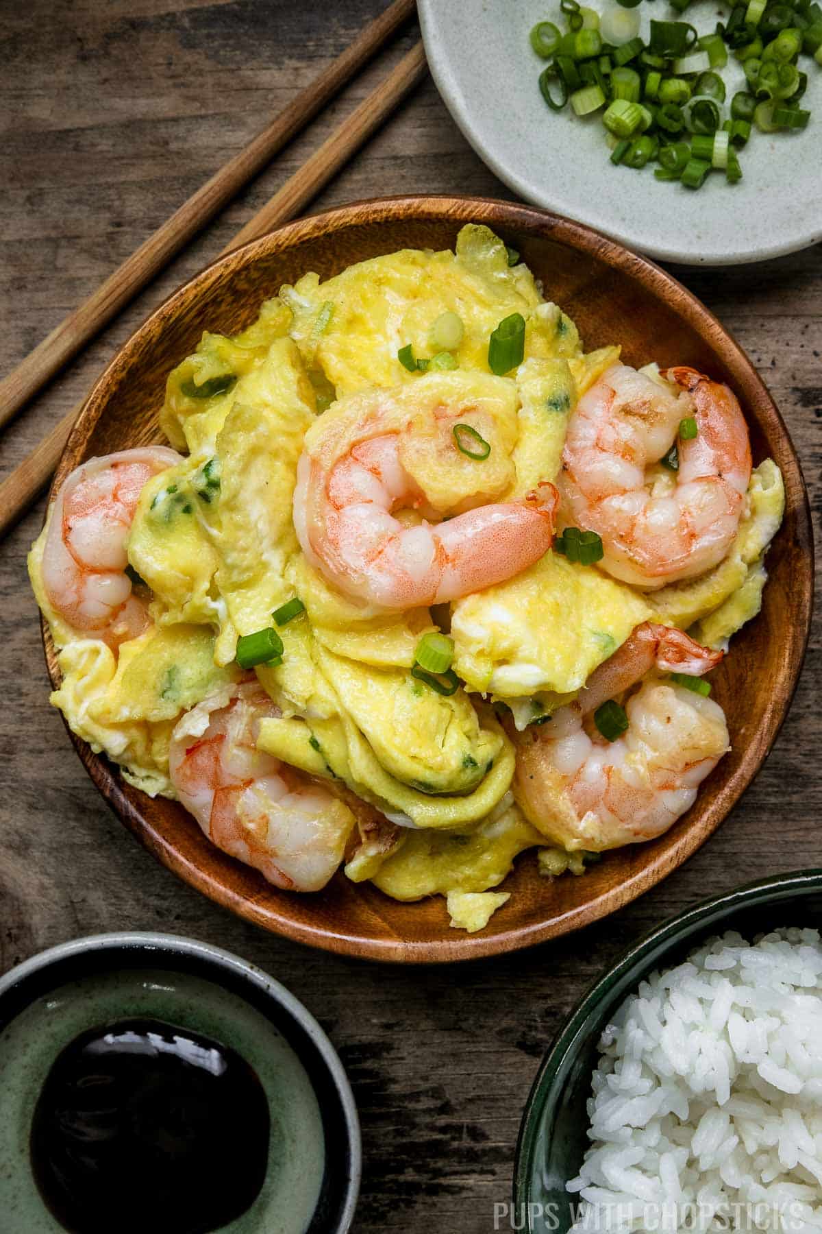 Chinese scrambled eggs and shrimp stir fry served on a wooden plate with a side of white rice