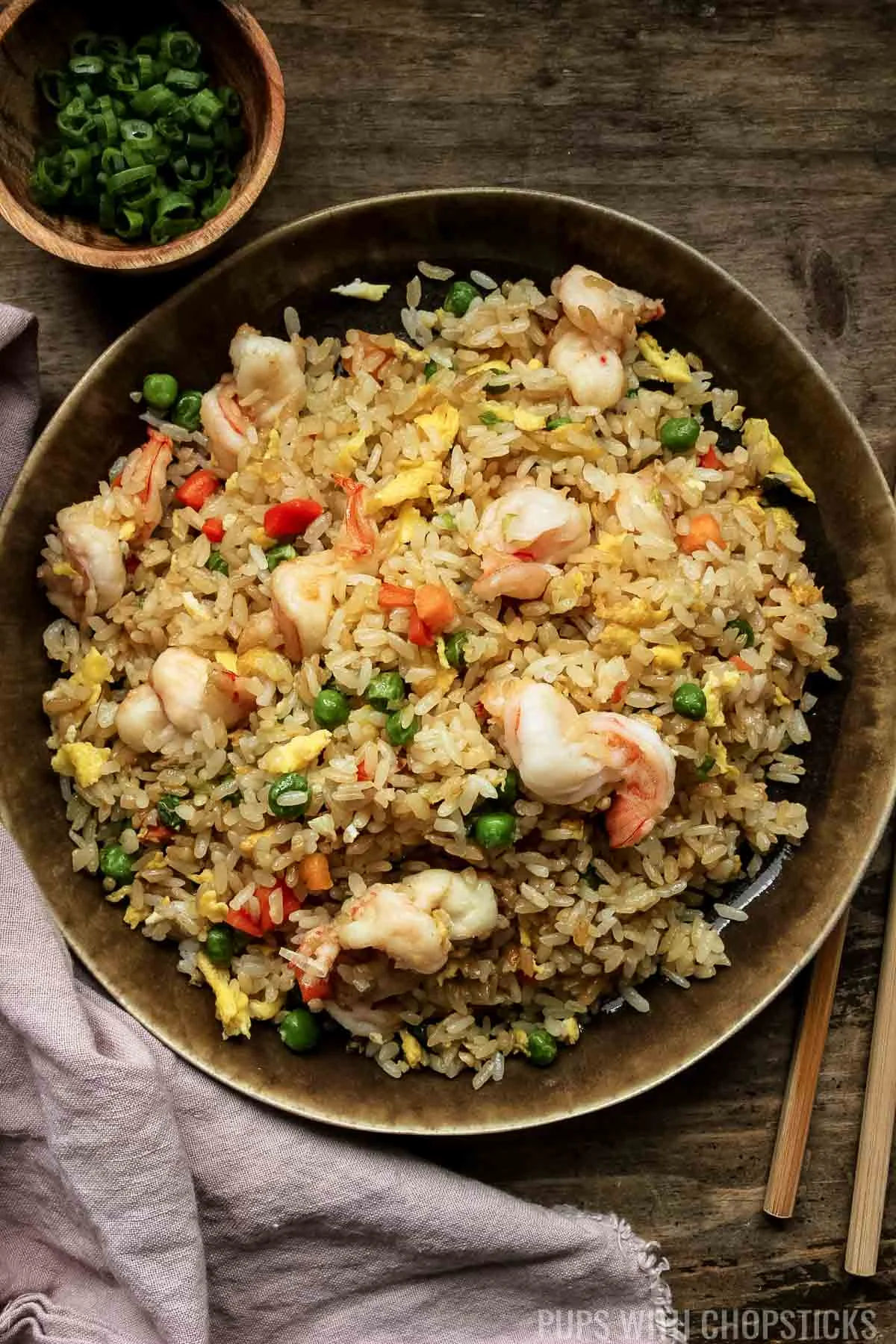 chinese shrimp fried rice on a brown plate with wooden chopsticks.