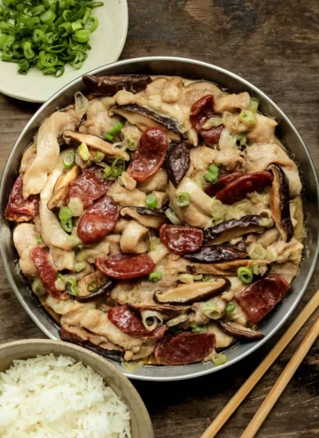 chinese steamed chicken with chinese sausage and shiitake mushrooms on a metal plate with a bowl of white rice.