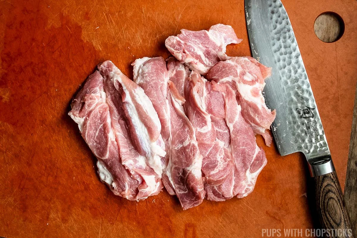 thinly slice pork shoulder on cutting board.