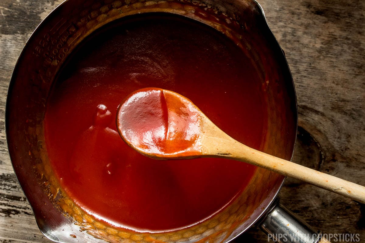 Sweet and sour sauce on wooden spoon to show it's thickness and red color.