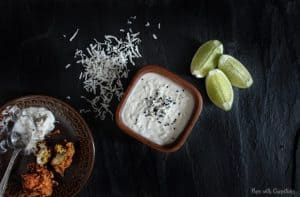 Creamy Coconut Dip in a small bowl with limes and coconut flakes on a table