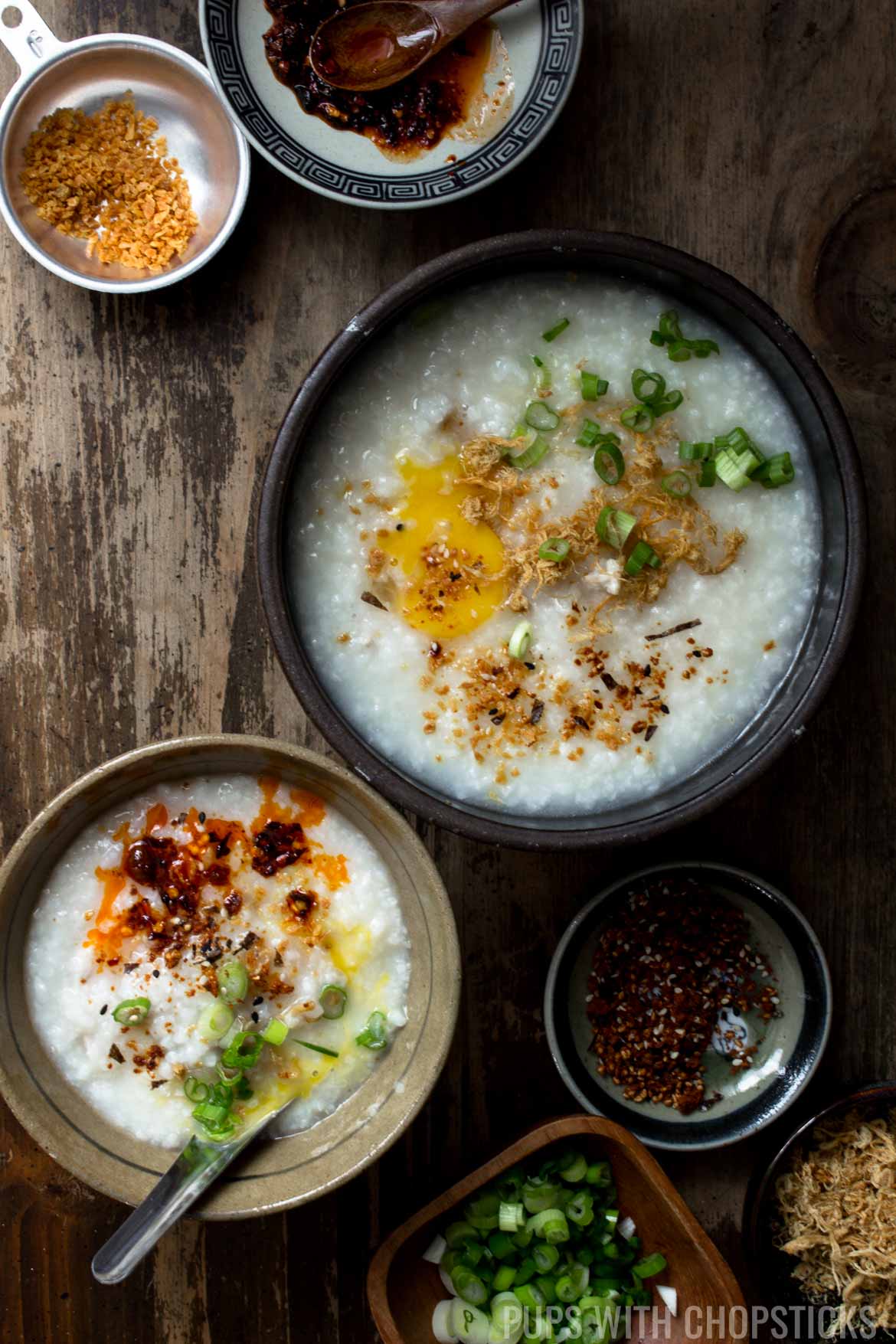 A large bowl of congee placed on a table with a few side dishes of toppings
