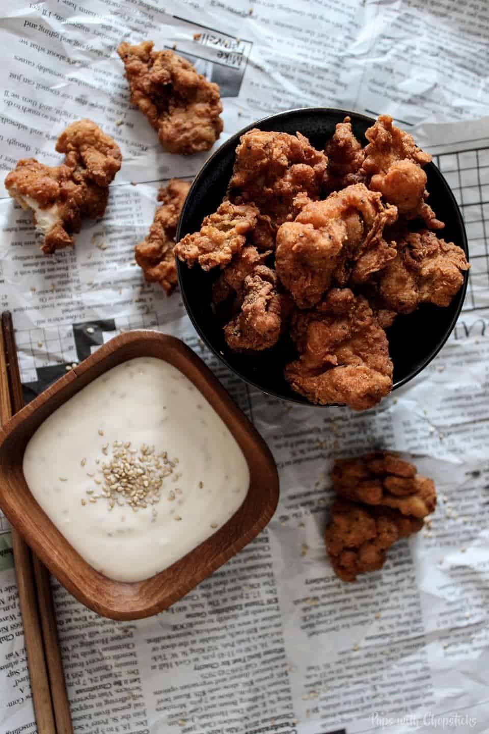 Topview of Crispy Buttermilk Popcorn Chicken with Creamy Honey Sesame Dip on a table laid out on newspaper