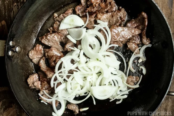 adding onions to beef in frying pan.