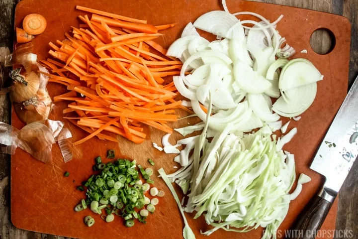 chopping board with chopped carrots, green onions, cabbage and onions.