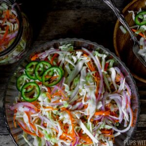 Curtido (Salvadoran Pickled Cabbage Slaw) in a large serving bowl served on a small wooden plate