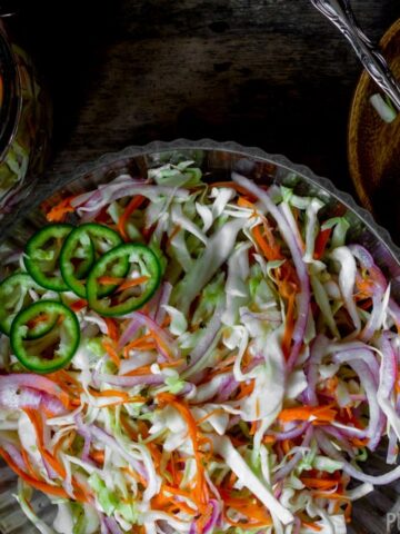 Curtido (Salvadoran Pickled Cabbage Slaw) in a large serving bowl served on a small wooden plate