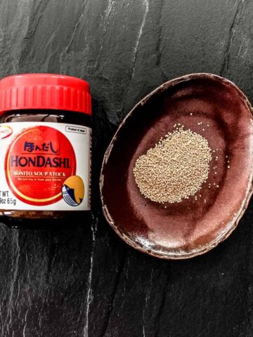 A bottle of dashi powder on a dark counter with dashi granules on a small plate