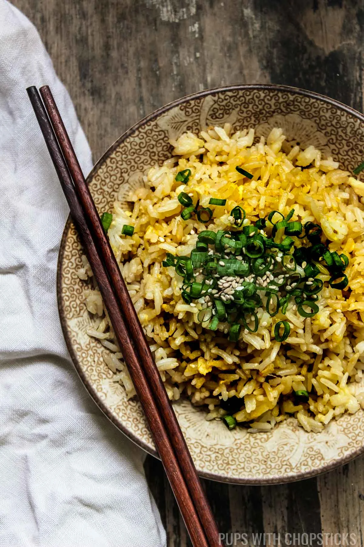 A large bowl of Chinese egg fried rice on a wooden table with a pair of chopsticks and a handkerchief