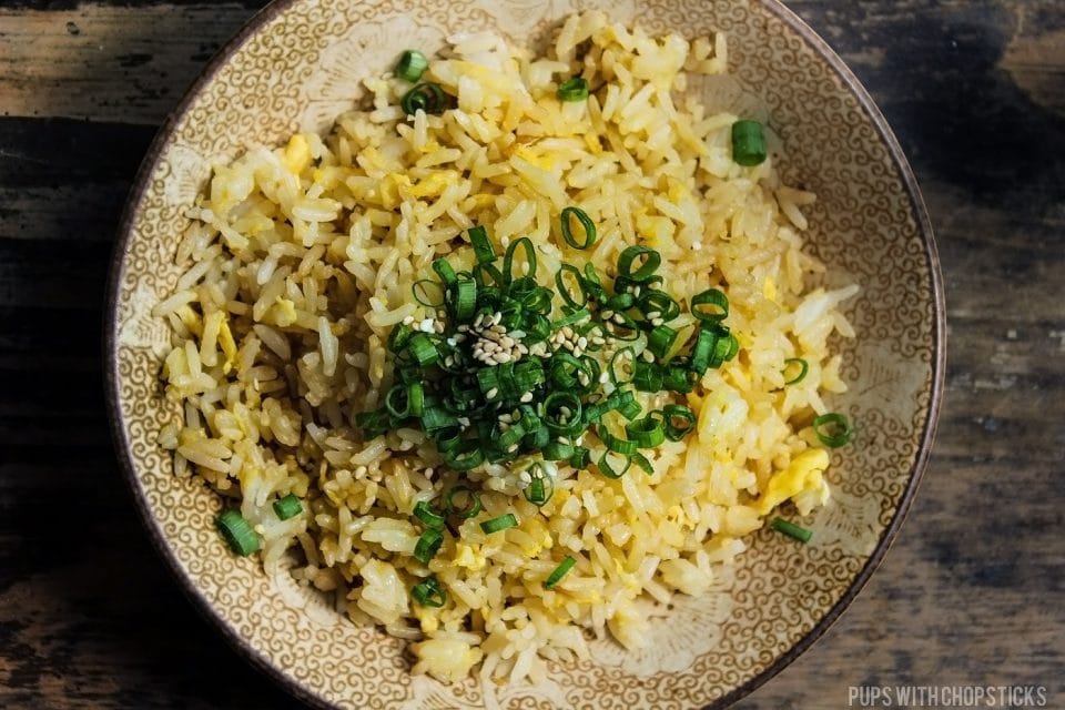 A large bowl of egg fried rice, topped with green onions and sesame seeds on a wooden table