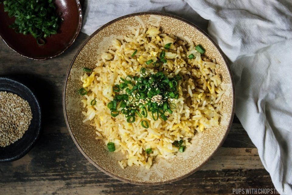 Egg fried rice, topped with green onions in a bowl on a wooden table with a handkerchief.