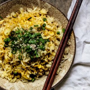Egg fried rice, topped with green onions in a bowl on a wooden table with a handkerchief.