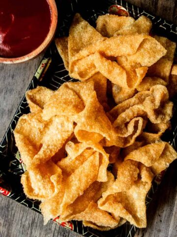 Chinese fried wonton strips on a takeout tray served with sweet and sour sauce