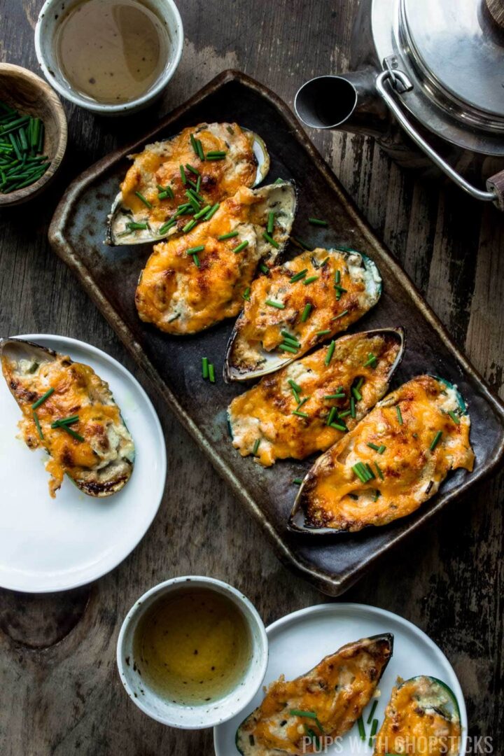 A plate of garlic cheese baked mussels being served with a side of tea