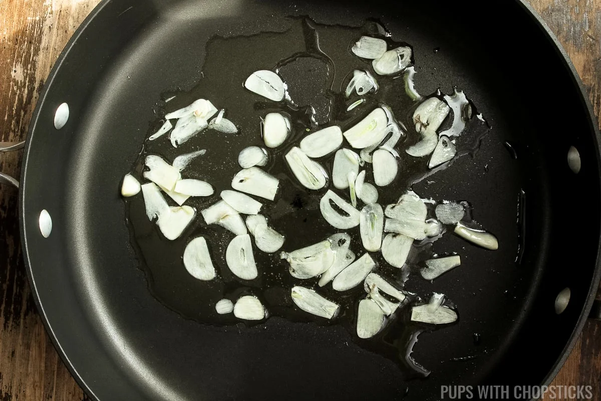 Thinly sliced garlic in a frying pan being fried.