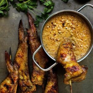 Baked curry chicken wings skewered and dipped in peanut sauce