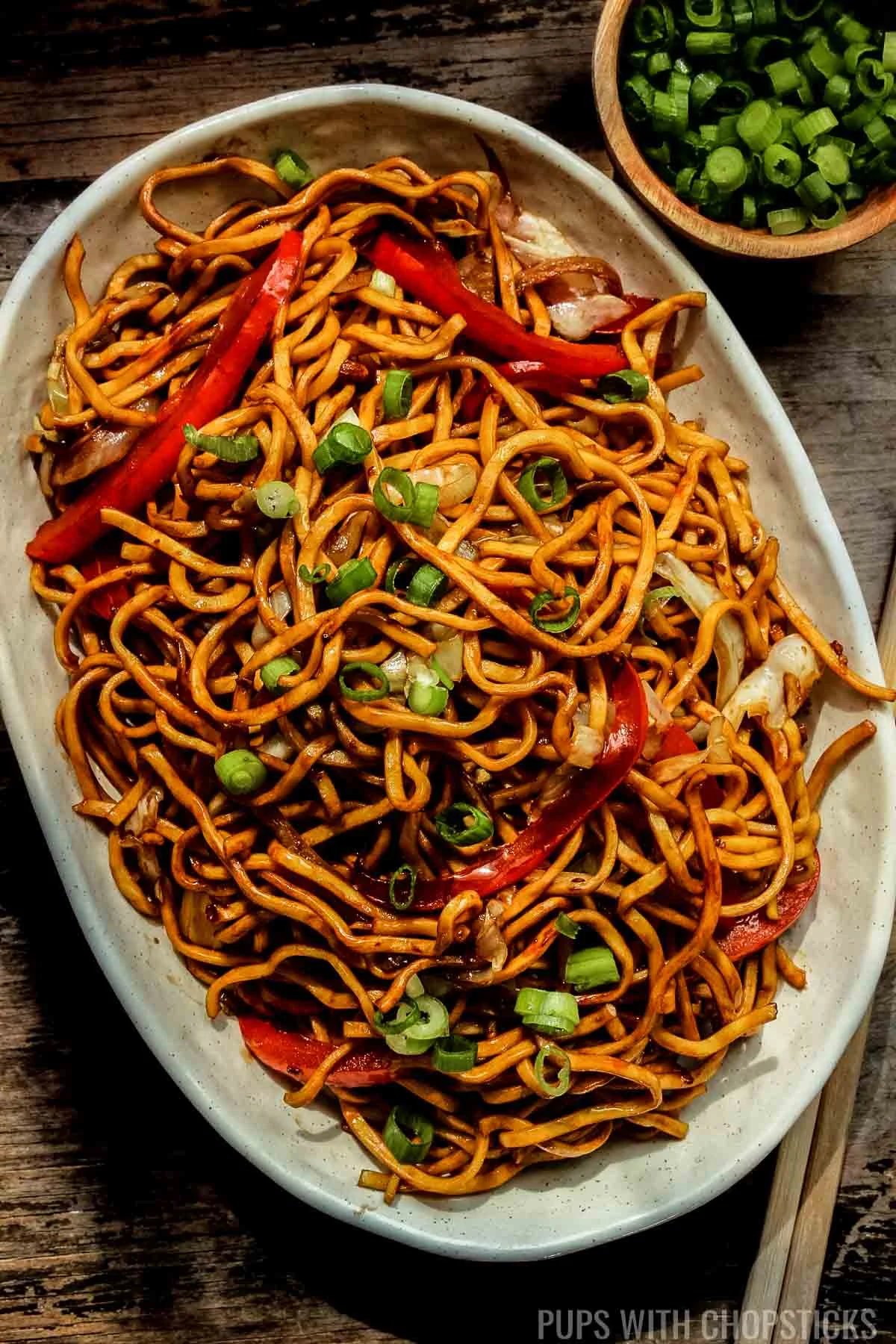 Hakka Noodles on a white plate served with green onions on the side.