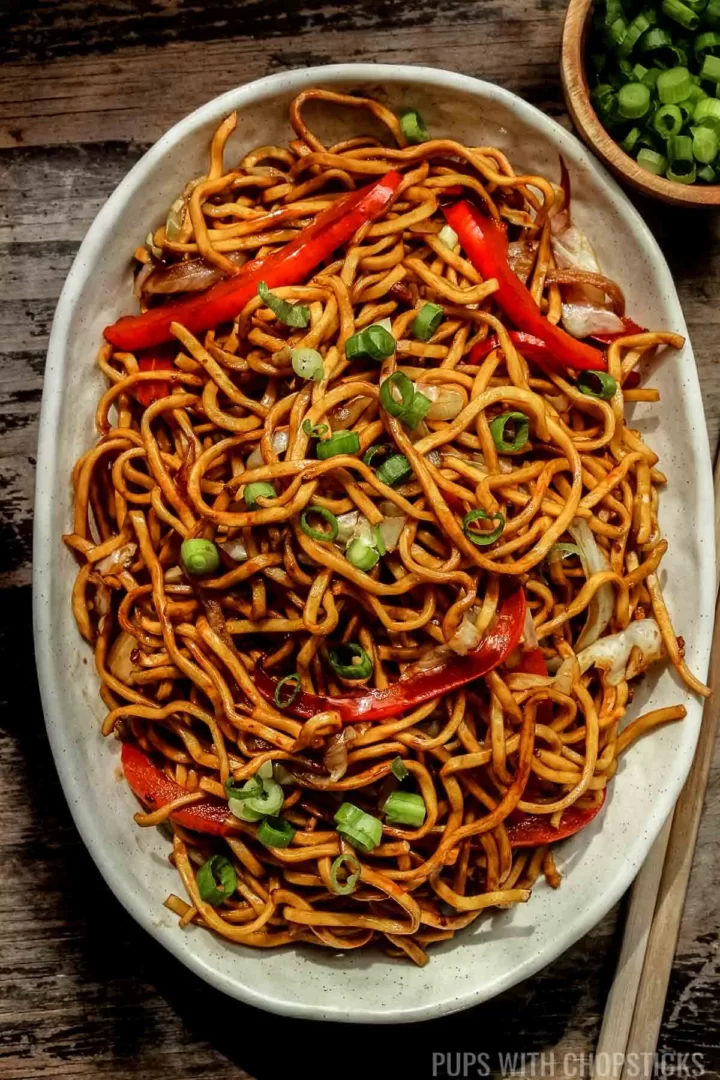 Hakka noodles on a white plate on a wooden table.