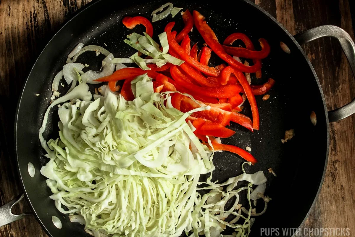 Frying pan with sliced red bell peppers, and cabbage being stir-fried.