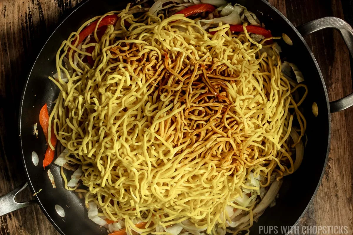 Frying pan with Hakka noodles and sauce being stir-fried.