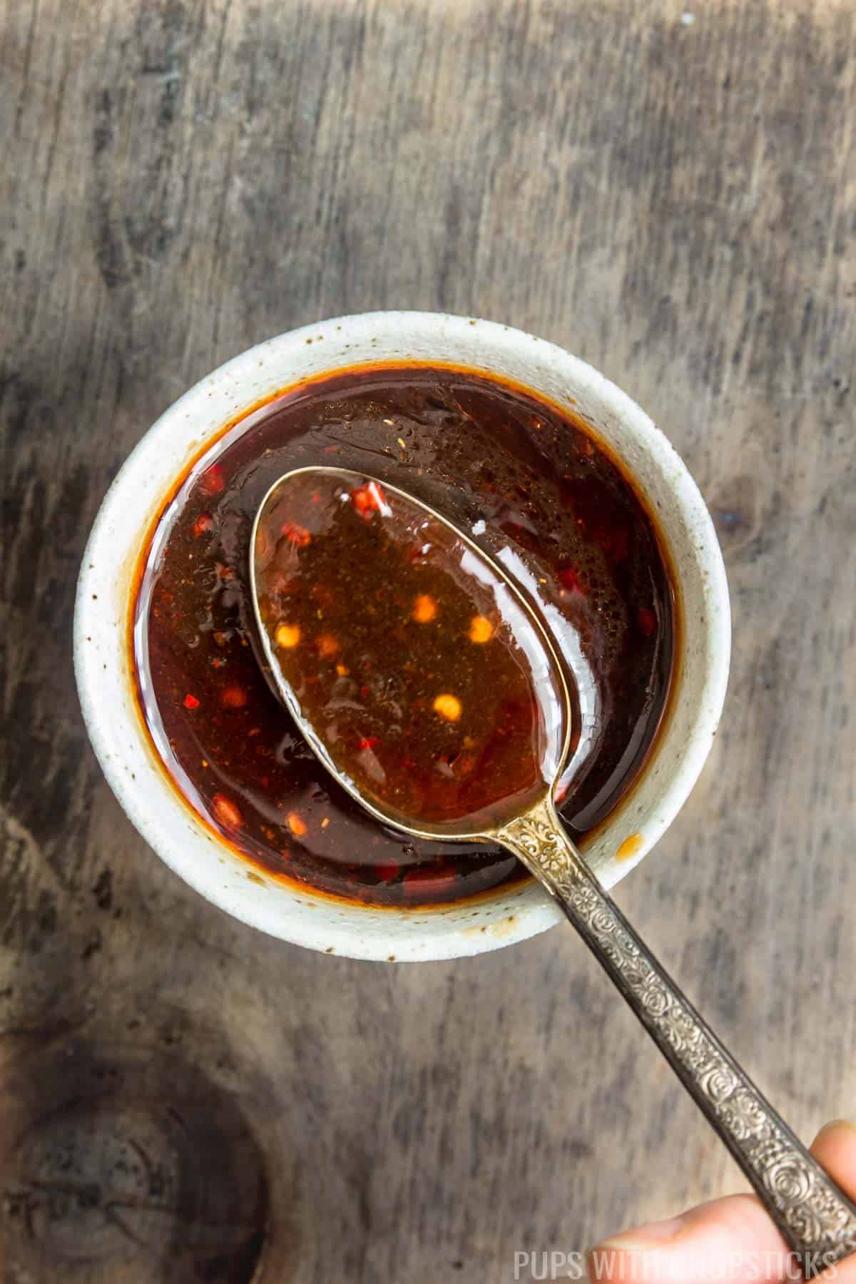 A close up of hoisin dipping sauce being shown with a metal spoon.
