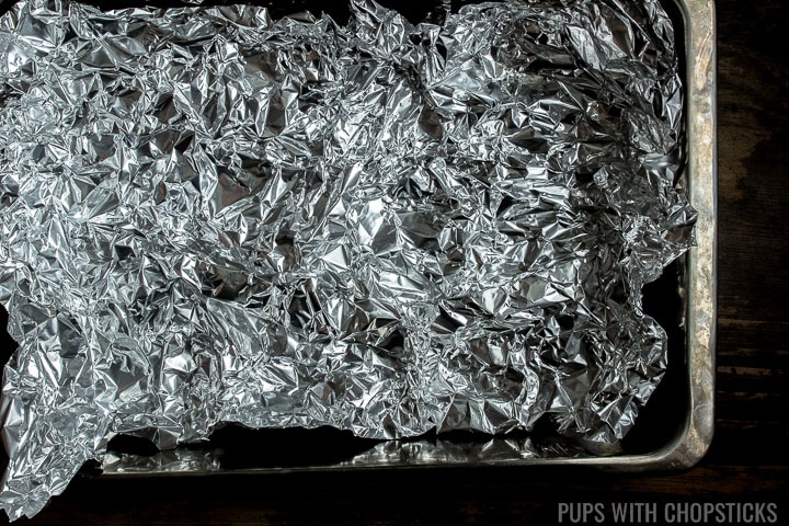 A metal pan, lined with crinkled up foil as a liner for the chicken