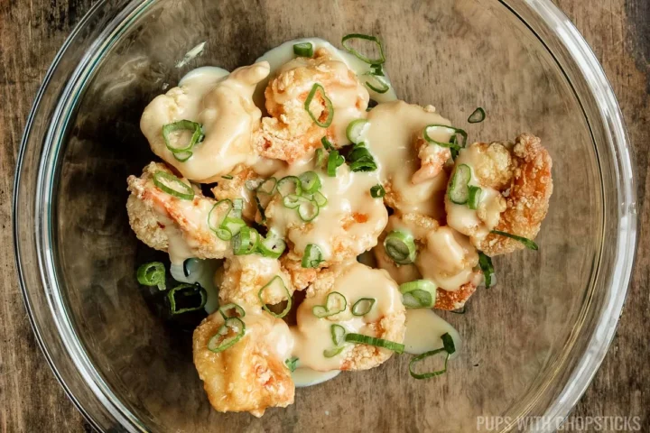 a glass bowl with deep fried shrimp, mayo sauce and green onions.