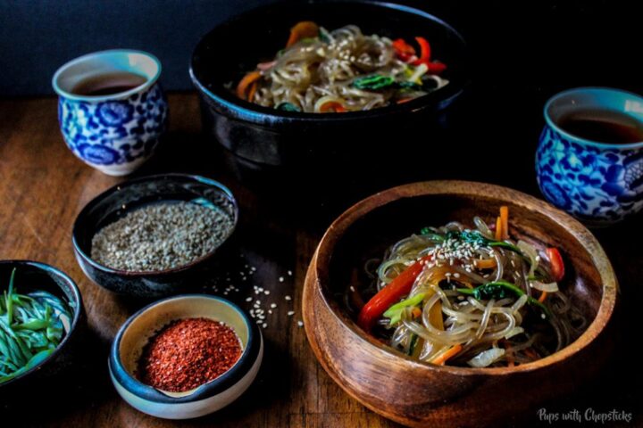 Chewy Korean Glass Noodles (Chap Chae/Japchae) in bowls on a table with tea and garnishes