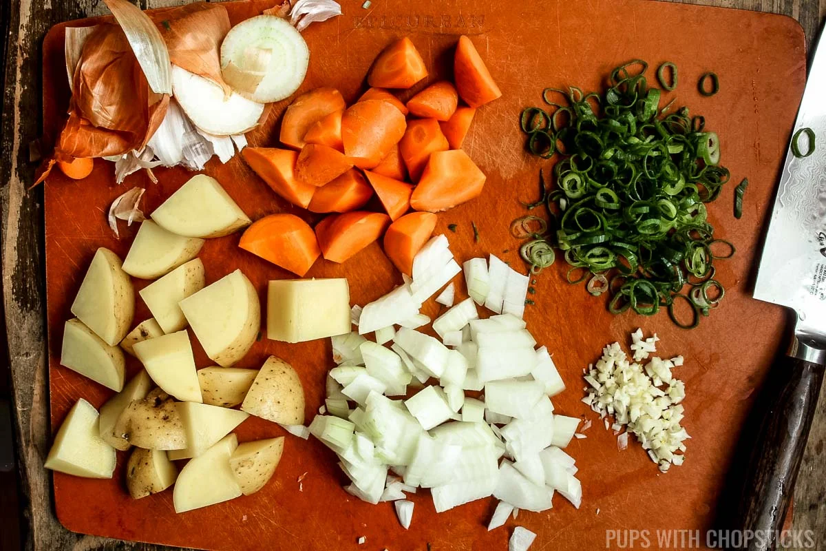 Chop carrots, potatoes, green onions, onions and garlic on a cutting board