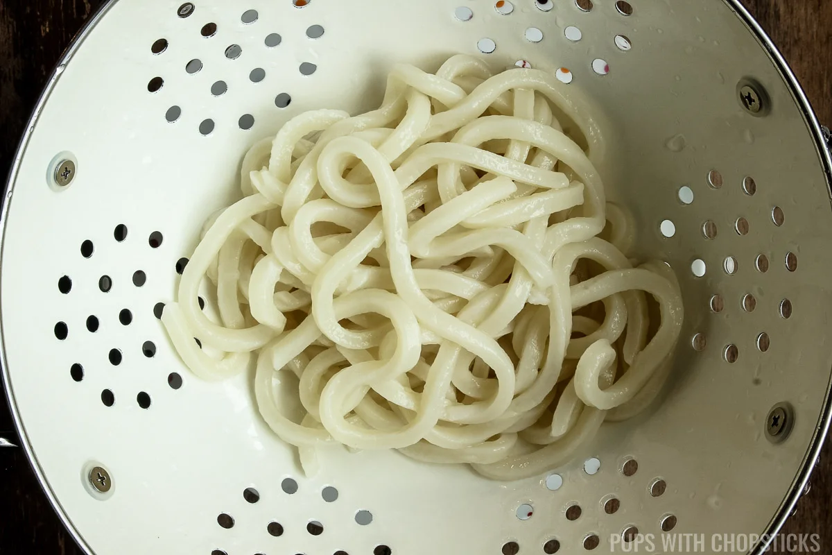 Thawing frozen udon noodles in a colander with cold water