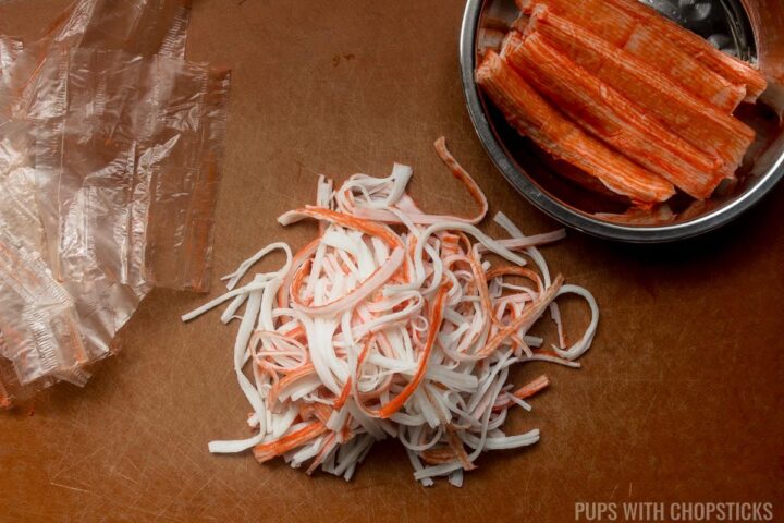 Imitation crab meat shredded into long strips, on a cutting board.