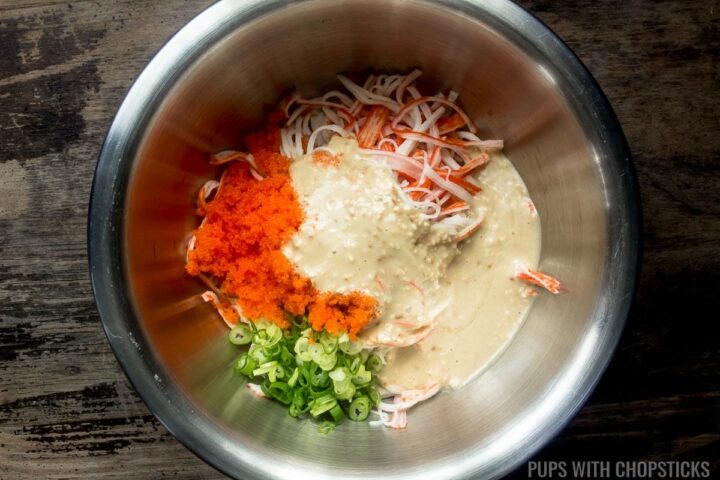 A large metal bowl with imitation crab meat, sesame kani dressing, green onions and tobiko, being ready to be mixed.