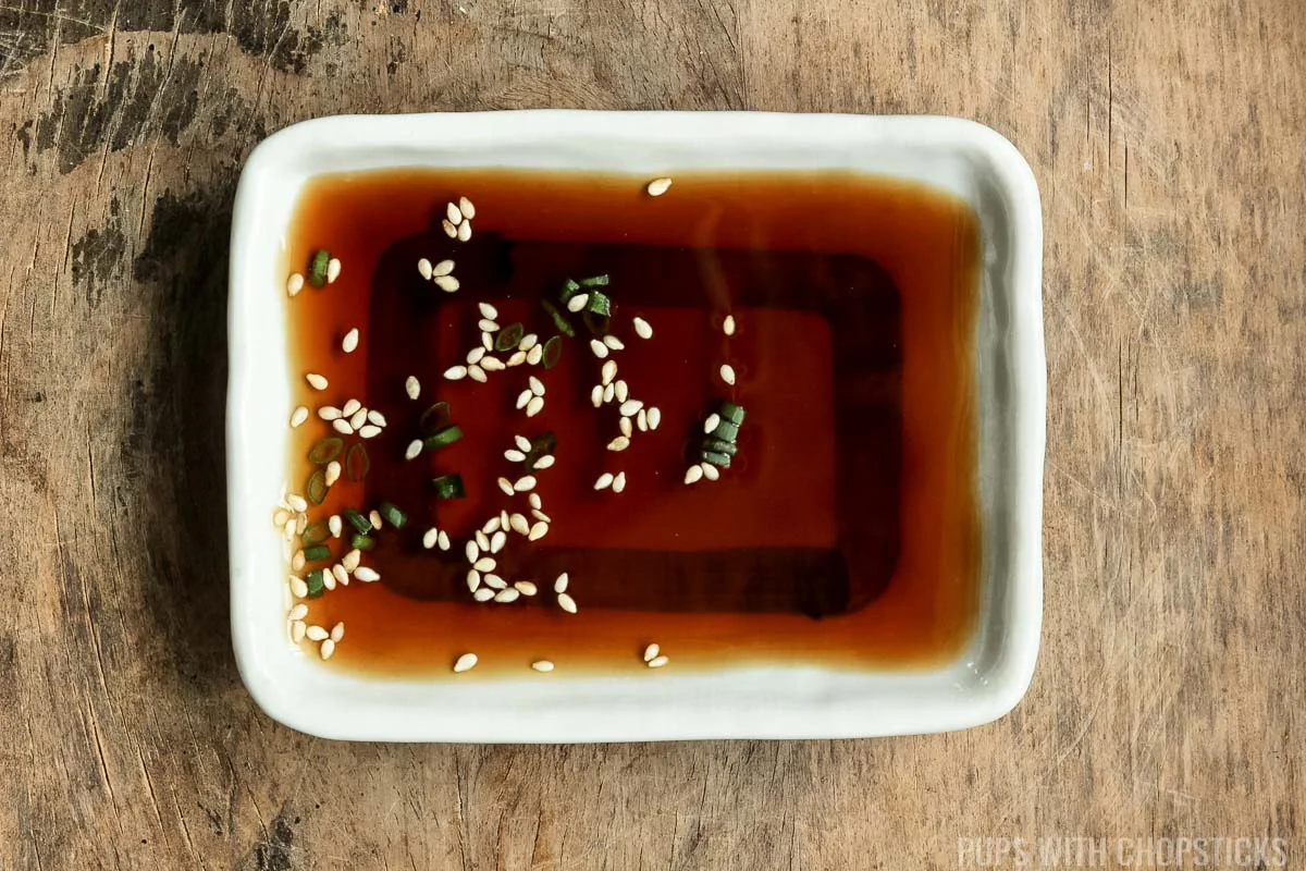 Homemade ponzu sauce in a small white bowl on a wooden table.