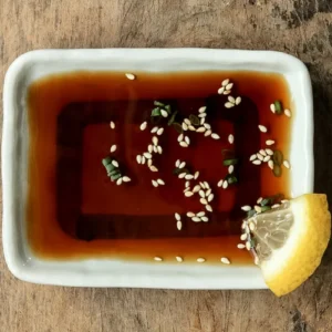 Homemade ponzu sauce in a small white bowl on a wooden table with lemon slice.
