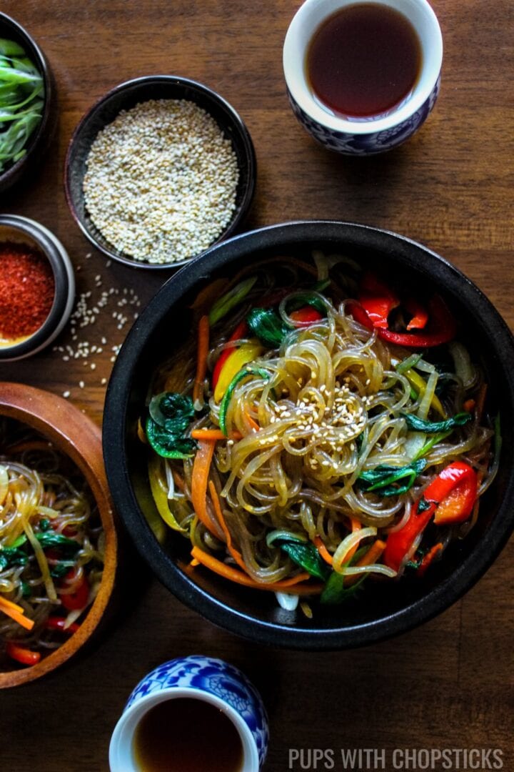 Bowls of Korean Glass Noodles ( Japchae / Chapchae ) with garnishes on a table